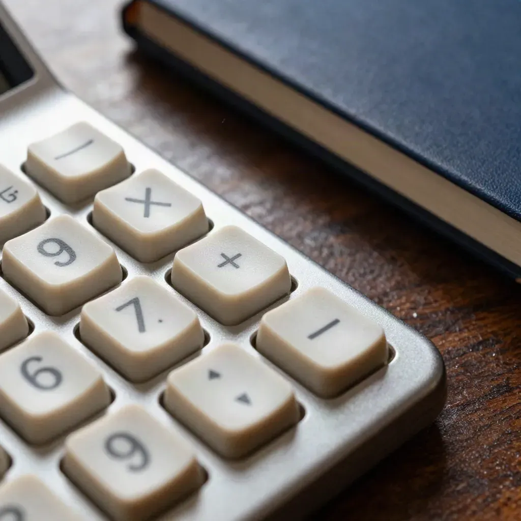 Extreme macro of a calculator keypad, keyring and navy notebook edge on dark wood.